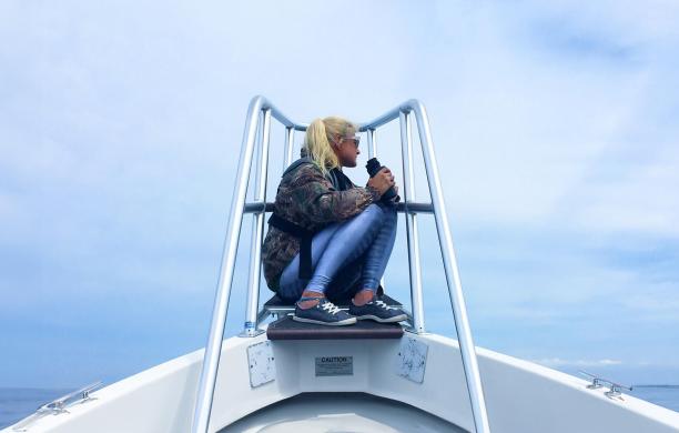 Brittany Bartlett sits at the bow of a boat while holding binoculars to survey Harbor Seals for the Navy.