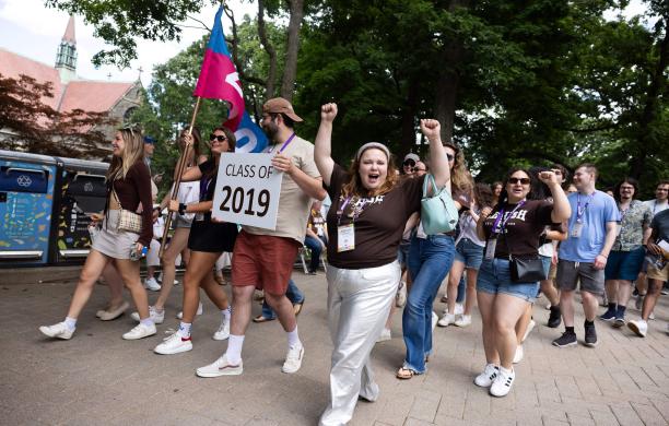 The Class of 2019 parades down the street, holding a 2019 sign while one woman cheers towards the camera with her hands.
