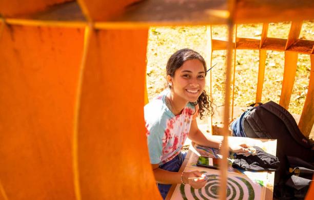 A student sitting within an orange sculpture with a drawing in their lap.