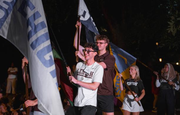 College students wearing tshirts carry tall flags in a parade.