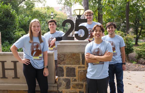 Students wearing blue Founder's Day t-shirts stand beside a structure of the number 25 standing on a wall, signifying this year's graduating class of 2025.