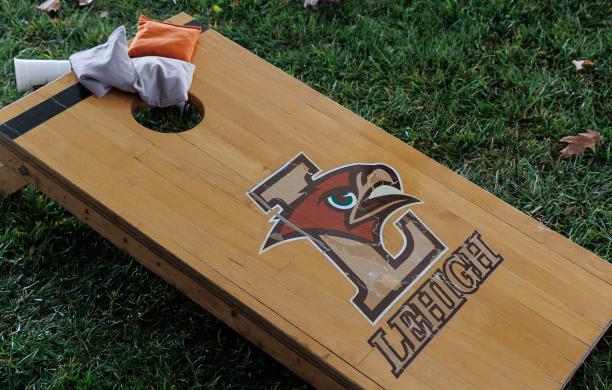 A wooden baggo board emblazoned with the Mountain Hawk logo sits on the grass with bean bags resting on the top of the board.
