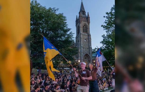Mark Shiner in a parade of alumni carries a flag for his class of 1977 with the bell tower of the University Center standing tall behind him.