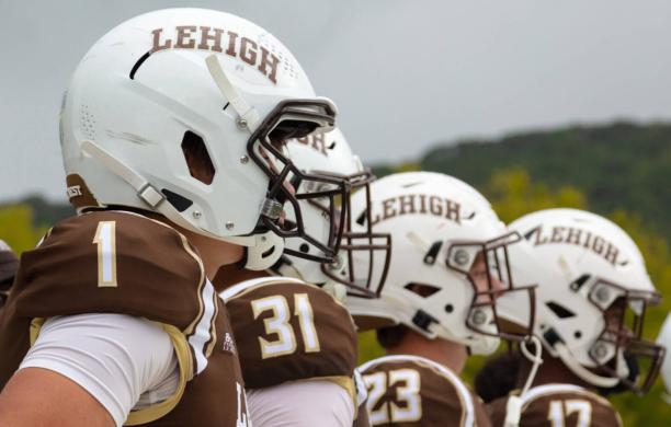 A row of football players line up for a view of their profiles and sides of their white helmets with the numbers on their shoulders facing the camera..