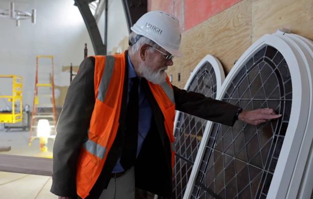 Beall Fowler stands in the former Asa Packer Ballroom and admires the refurbished stained glass windows, touching one.