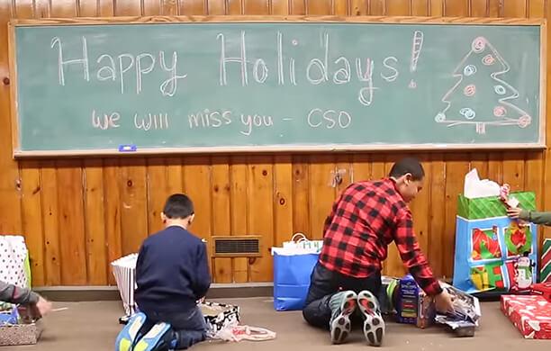 Children opening gifts beneath a chalkboard reading Happy Holidays