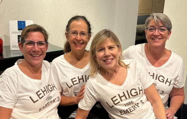 Four women sit closely together smiling while wearing the same white tshirt that says "Lehigh 1986 Emery 3".
