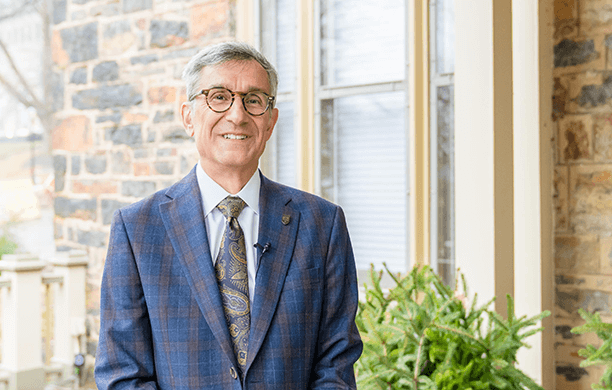 Lehigh president Joseph Helble, dressed in a suit and tie, stands on the porch of the President's House at Lehigh University.