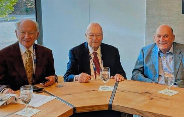 Herb Roemmele, Bob Gill, and Arthur Tauck Jr. sit at a table wearing suits and ties with glasses of water in front of them.