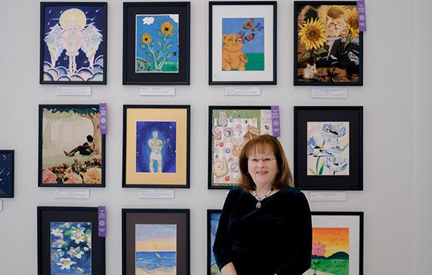 Heather Rodale '74 stands in front of three rows of student created art