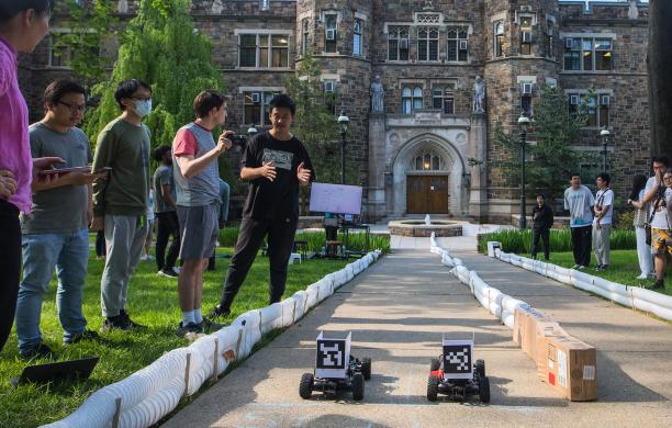 A race track is set up on the pathway in front of Packard Lab with small race cars competing   as competitors and spectators watch on from either side.