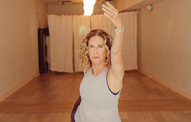 Kyle Greenberg '85 in a yoga studio raises her arm and holds her foot in a yoga pose