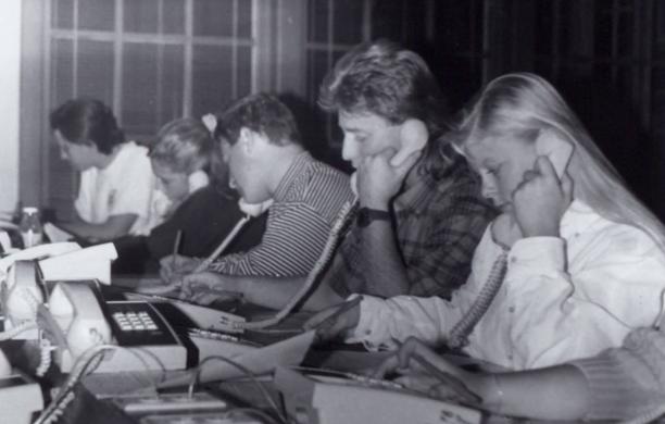 A long table of male and female students seated with push button telephones, focused on their task.