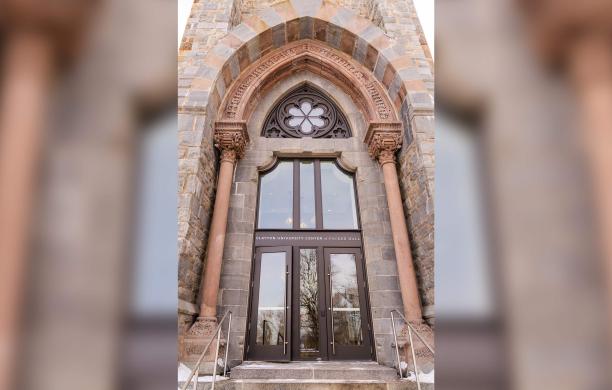 An upward angle of the tall, arched, stonework entry of the Clayton UC with a “Clayton University Center at Packer Hall" sign above the double glass doors. 