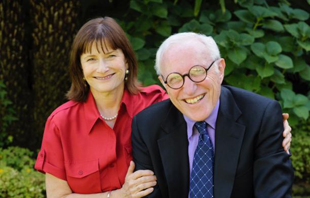 Nancy Berman sits beside her father with one arm behind him and holding his left arm with her left hand while both smile outdoors.