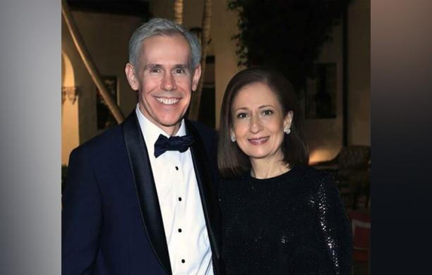 John Chrin wears a classic tuxedo beside Maria Chrin wearing a black, sleek, formal dress and a short straight bobbed hairstyle.