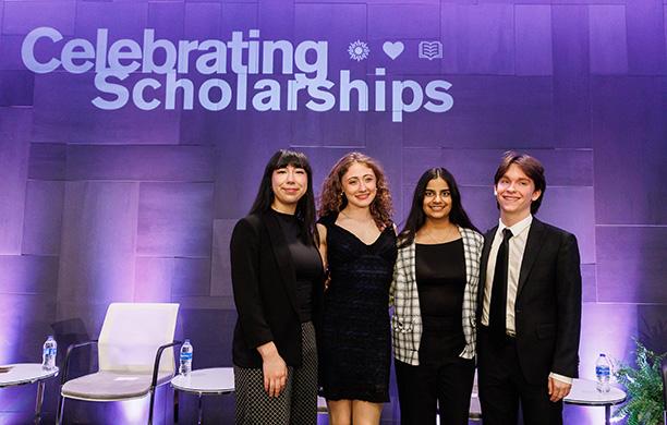 Four students stand together on a platform stage with a purple backdrop