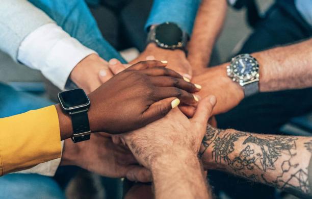 A closeup of hands of different ethnicities and sleeves with different styles joined in the center, one on top of the other.
