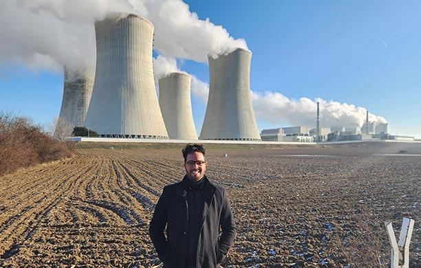 Eddie Guerra stands in a field in front of a nuclear power plant in the Czech Republic 