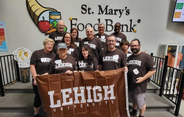 Alumni stand together wearing brown Lehigh t-shirts while holding a Lehigh flag.