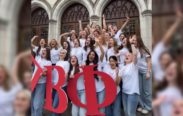 Members of Pi Beta Phi wearing matching white shirts and holding big red Greek letters, cheer with excitement and hands raised.