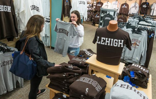 Daughter holds up a gray shirt that says "Lehigh" in brown lettering while mom admires it amid racks of Lehigh clothing.