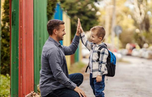 A father kneels at eye level with his son to give him a high five.