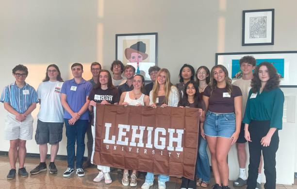  A group of 16 smiling people holding a Lehigh banner indoors.