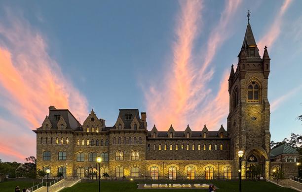 Stone university building lit up in front of the evening sky.