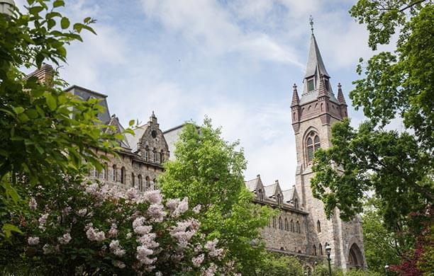 Shot of the Clayton University Center on a clear day; pink flowers and vivid greenery in the foreground.