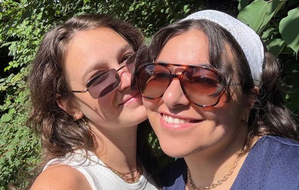 Claudia and Ally press close together and smile. They stand outside with the sun shining on them; both wear sunglasses.