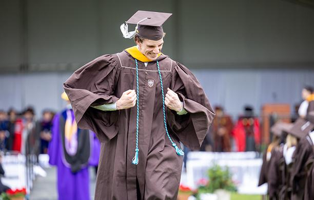 2025 Undergraduate wearing his brown cap and gown and teal Promise cord pumps his fists at Commencement