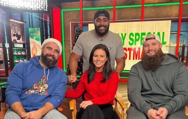 Kendall sits in the news studio with Lane Johnson, Jason Kelce, and Jordan Mailata. She wears a bright red sweater and white shoes.
