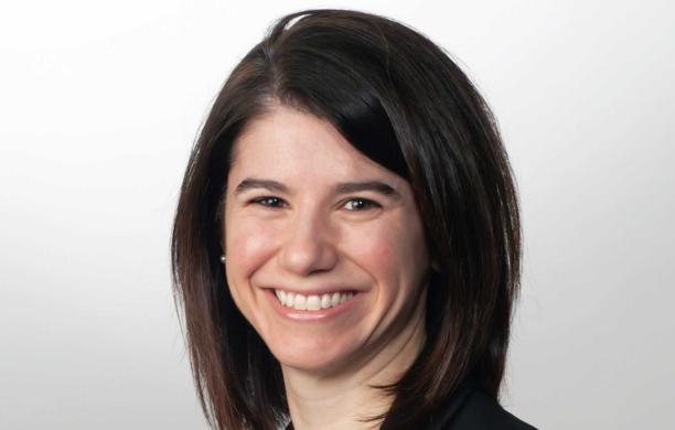 Christina smiles while wearing a black blazer, white shirt, and a silver necklace.