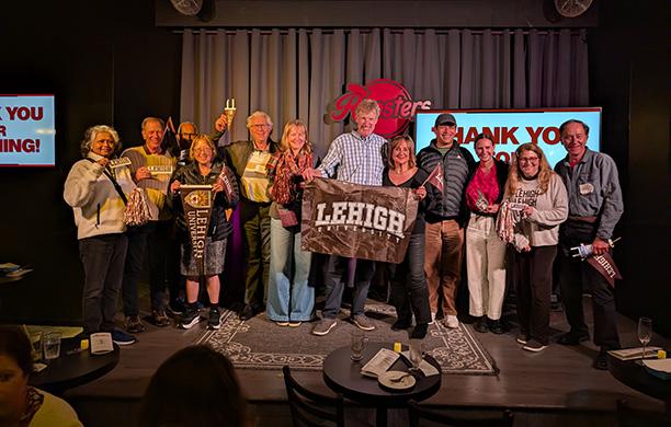 Don McMillan holds a Lehigh flag on stage at Rooster T. Feathers with Lehigh alumni