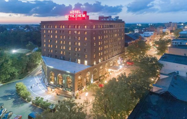 The Hotel Bethlehem against the backdrop of a cloudy evening. The neon sign on the roof glows red.