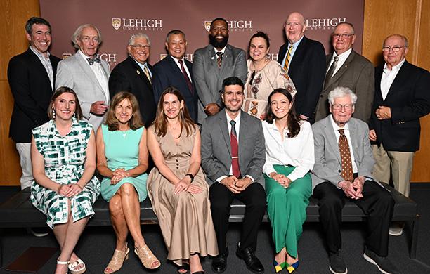 A group of Lehigh alumni sit and stand in front of a Lehigh banner