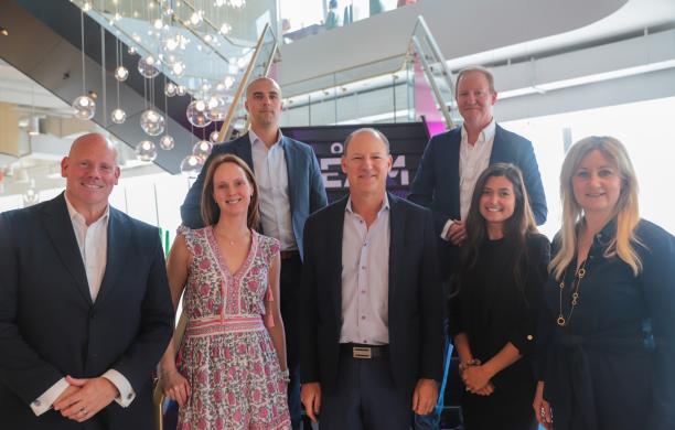 A group of alumni stand together on the steps at L'Oreal HQ. Dangling light fixtures create a warm glow.