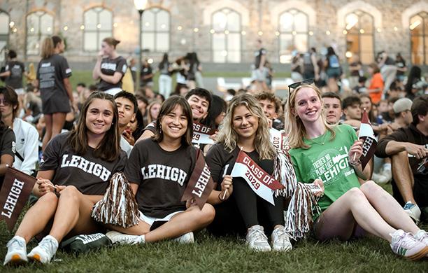 Four women in Lehigh t shirts sit on the lawn at the Rally