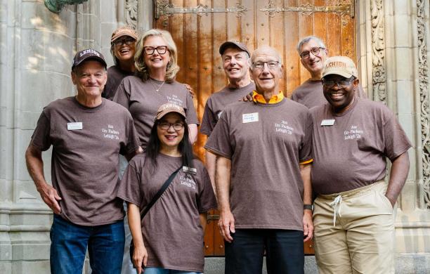 The volunteers stand together, smile, and wear matching brown shirts labelling them as Asa Un-Packers. 