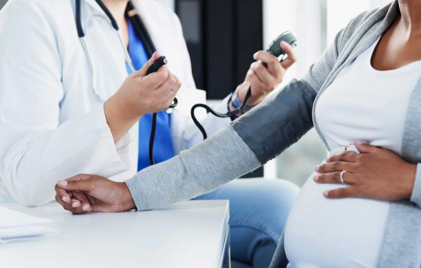 A woman in a white coat holds a stethoscope and reaches out to a pregnant woman.  