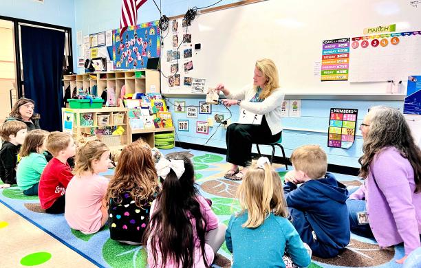 Bridget sits in a classroom amid a group of pre-K students with a book in her lap. She shows them a photo.