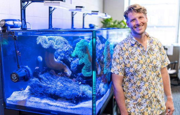Patrick stands alongside a large aquarium with the VorTech propeller pump on display. He wears a bright floral shirt.
