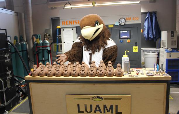 Clutch stands in front of a row of brown Quackers in the Design Lab and gestures to them.