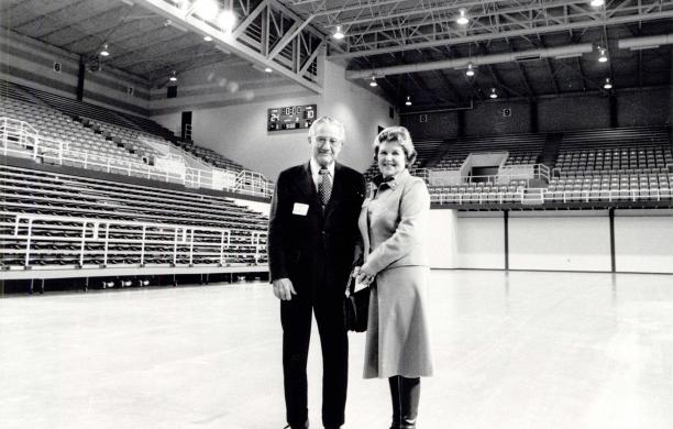 Donald and Dorothy wear business attire and stand together on a basketball court post-game. A scoreboard is visible behind them.