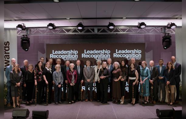 The recipients stand together alongside President Helble in the center. They all wear business attire and hold their awards.