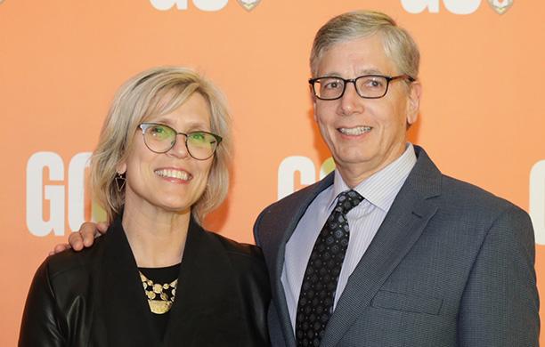 A couple in business attire stand in front of an orange background