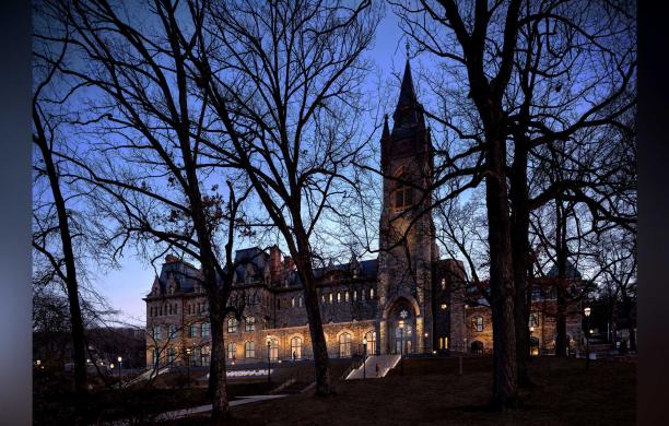 An evening shot of the Clayton University Center as seen between a group of bare trees in the foreground.