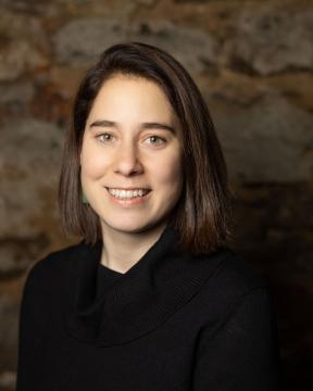 A woman smiles wearing a black sweater in front of a dark background