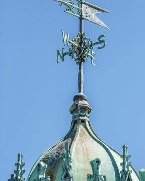 A tarnished weathervane backed by a bright blue sky
